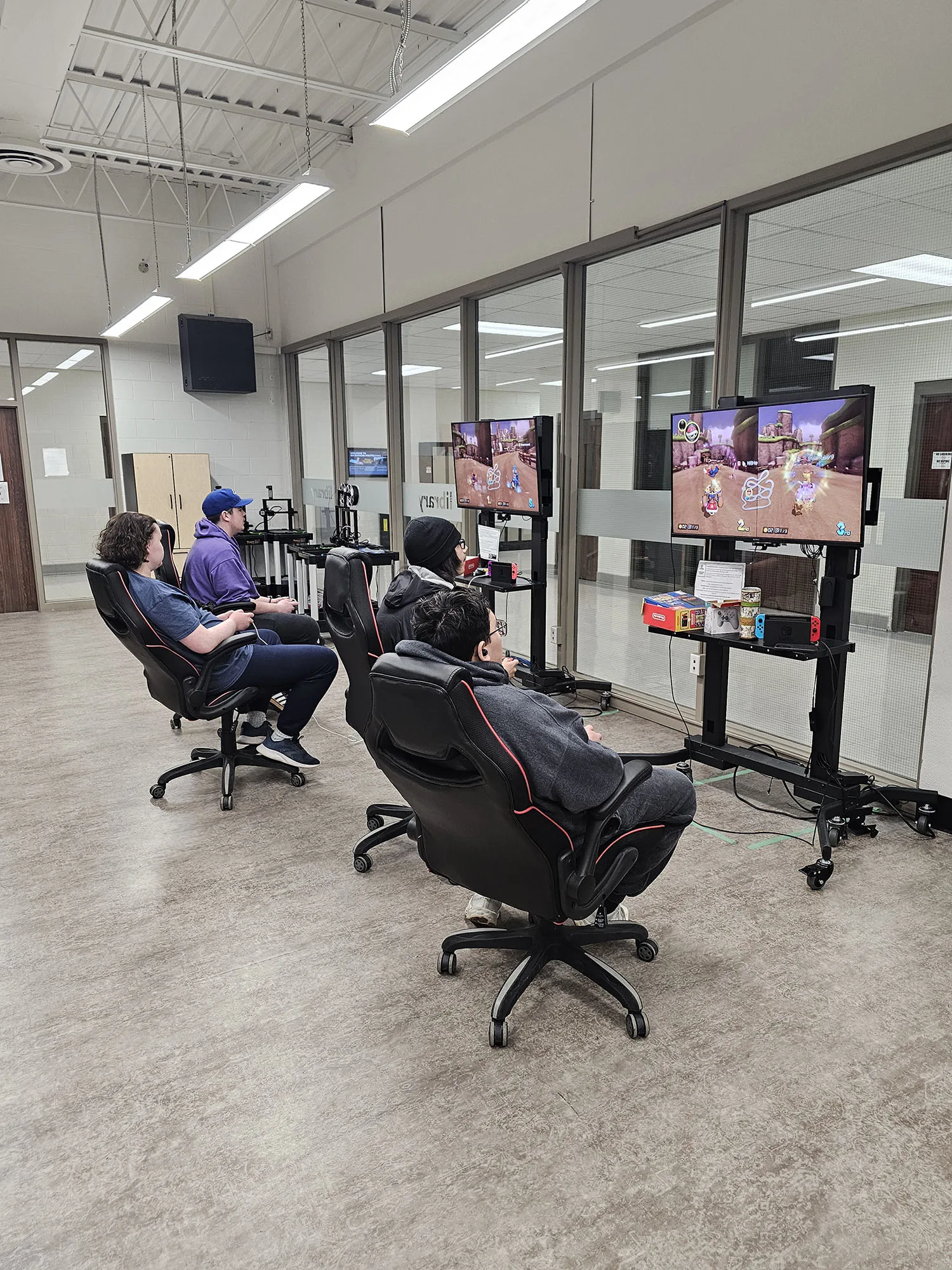 students sitting in office chairs and playing mario kart as an e-sport on large monitor screens