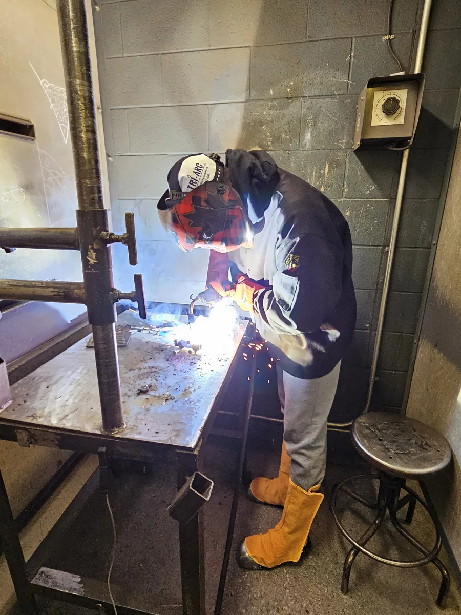 student in Welding Level 1 OYAP program at SNP Secondary School wearing protective gear and using a welding torch